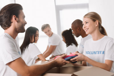 Group of cheerful young volunteers packing food and supplies into cardboard boxes in a bright room.