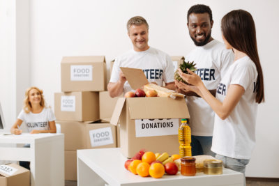 Group of cheerful young volunteers packing food and supplies into cardboard boxes in a bright room.