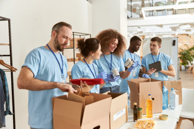 Group of cheerful young volunteers packing food and supplies into cardboard boxes in a bright room.